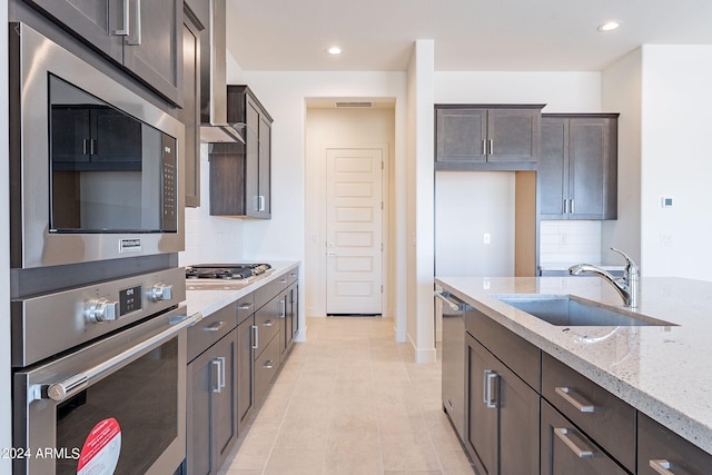 kitchen featuring dark brown cabinetry, sink, tasteful backsplash, appliances with stainless steel finishes, and light stone countertops