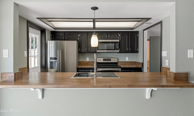 kitchen with stainless steel appliances, butcher block countertops, hanging light fixtures, and sink