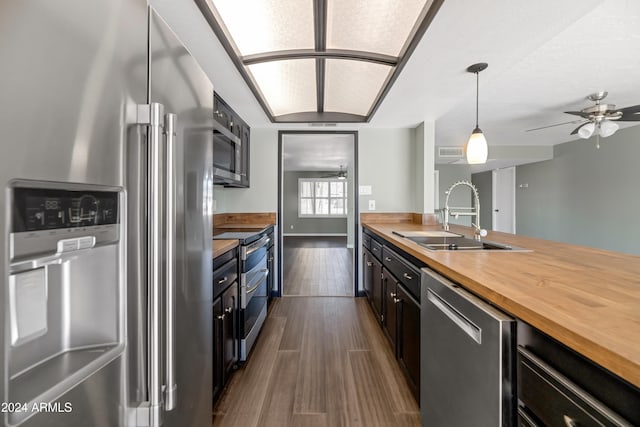 kitchen with appliances with stainless steel finishes, dark wood-type flooring, sink, pendant lighting, and butcher block counters