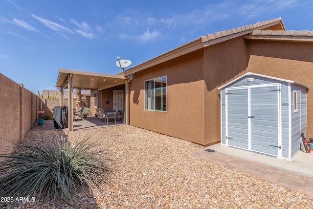 rear view of property with a shed, stucco siding, a fenced backyard, an outdoor structure, and a patio area