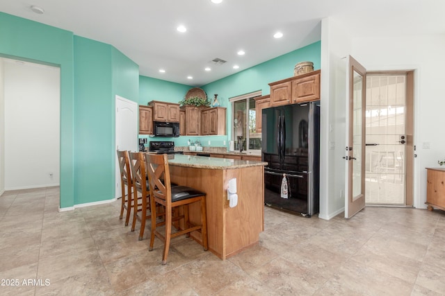 kitchen with light stone counters, visible vents, a kitchen island, black appliances, and a kitchen breakfast bar