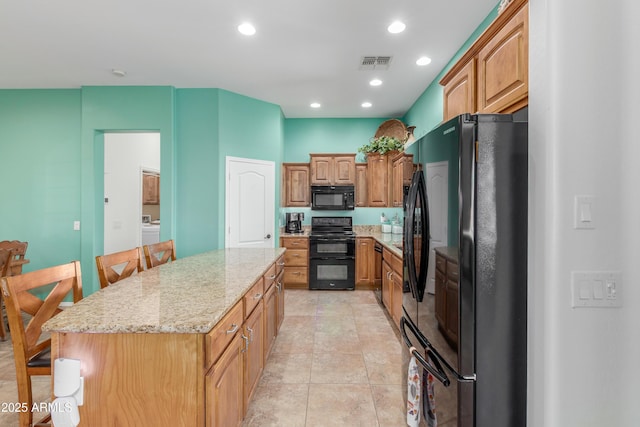 kitchen with light stone counters, visible vents, recessed lighting, black appliances, and a center island