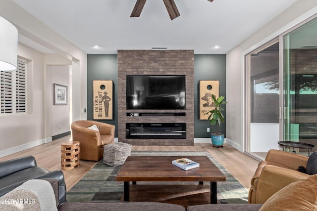 living room featuring ceiling fan, a fireplace, and light hardwood / wood-style flooring