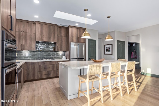 kitchen with hanging light fixtures, stainless steel appliances, a center island, tasteful backsplash, and light wood-type flooring