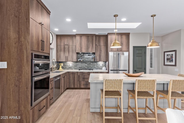 kitchen with a kitchen bar, sink, a skylight, appliances with stainless steel finishes, and pendant lighting