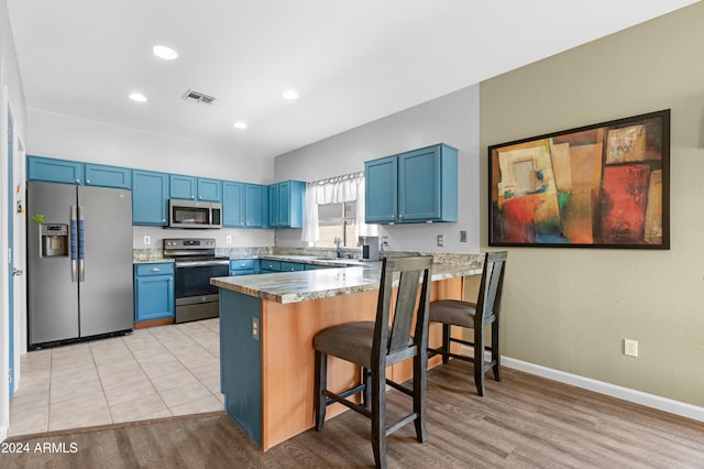 kitchen featuring light hardwood / wood-style flooring, blue cabinetry, stainless steel appliances, a kitchen bar, and kitchen peninsula