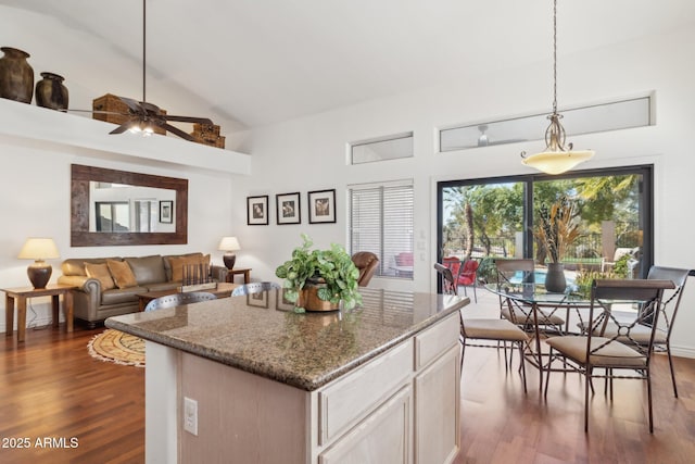 kitchen featuring pendant lighting, high vaulted ceiling, a kitchen island, dark hardwood / wood-style flooring, and dark stone counters