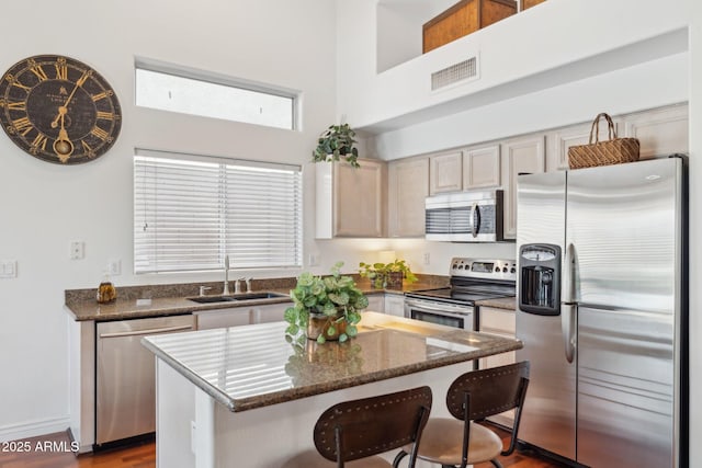 kitchen with sink, a breakfast bar, stainless steel appliances, a kitchen island, and light brown cabinets