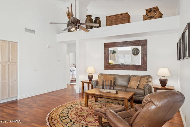 living room featuring hardwood / wood-style flooring, ceiling fan, and a towering ceiling