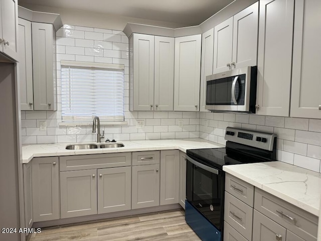 kitchen with light stone counters, sink, light hardwood / wood-style flooring, appliances with stainless steel finishes, and decorative backsplash