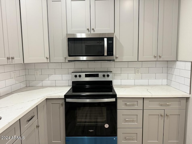 kitchen with appliances with stainless steel finishes, gray cabinetry, light stone counters, and backsplash