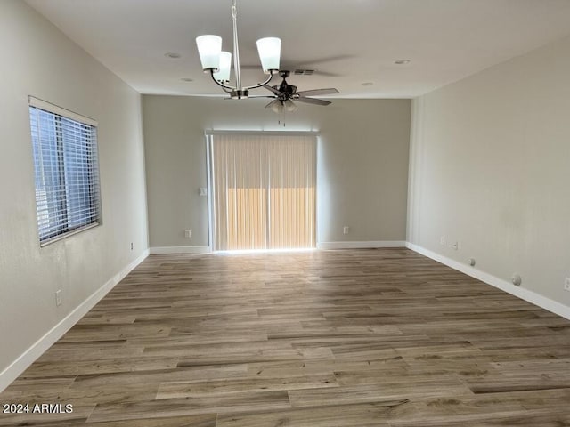 spare room with wood-type flooring and ceiling fan with notable chandelier