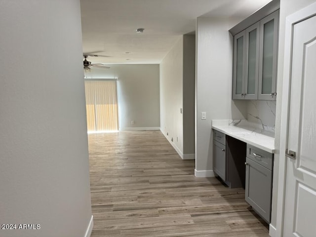 interior space with gray cabinetry, ceiling fan, light hardwood / wood-style flooring, and tasteful backsplash