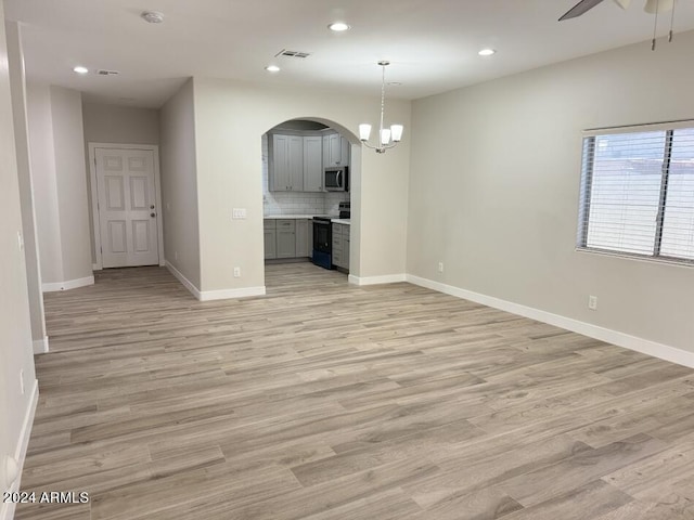 unfurnished living room with ceiling fan with notable chandelier and light hardwood / wood-style floors