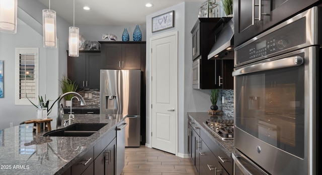 kitchen featuring sink, hardwood / wood-style flooring, appliances with stainless steel finishes, dark stone countertops, and decorative light fixtures