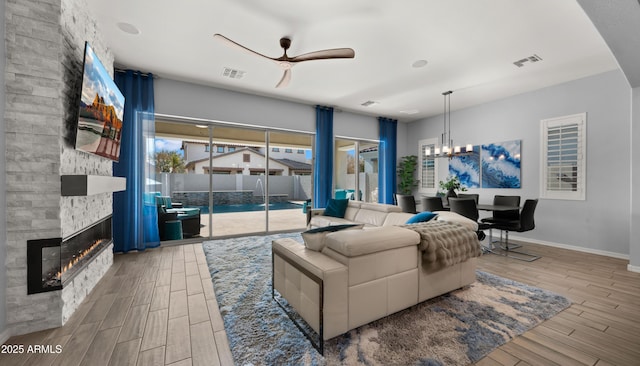 living room featuring ceiling fan with notable chandelier, a fireplace, and light hardwood / wood-style floors