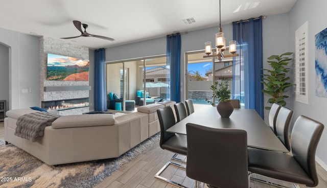 dining area with a stone fireplace and ceiling fan with notable chandelier