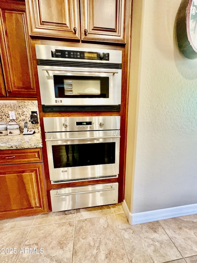 9249 E Desert Arroyos St, Scottsdale, AZ 85255 - kitchen with a warming drawer, stainless steel double oven, baseboards, light stone countertops, and brown cabinetry