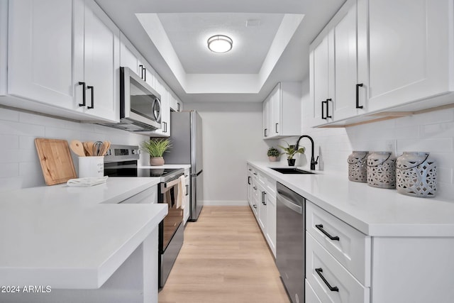 kitchen featuring white cabinets, a raised ceiling, sink, light hardwood / wood-style flooring, and stainless steel appliances