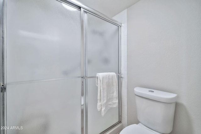 bathroom featuring a shower with shower door and toilet