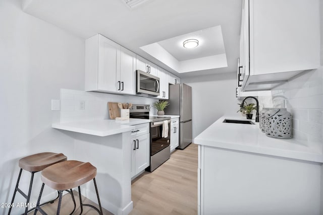 kitchen featuring appliances with stainless steel finishes, light wood-type flooring, sink, white cabinetry, and a breakfast bar area