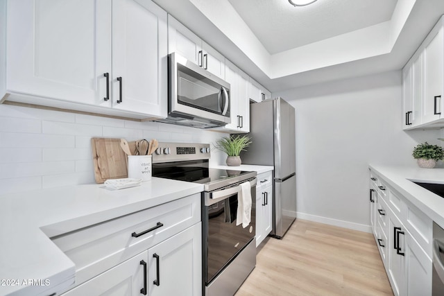 kitchen featuring decorative backsplash, appliances with stainless steel finishes, light wood-type flooring, and white cabinetry