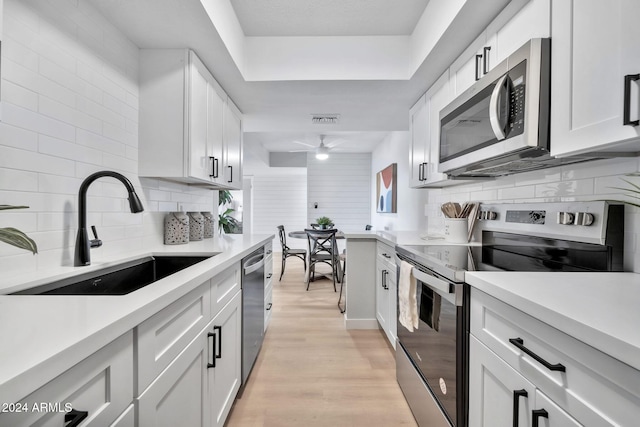 kitchen featuring appliances with stainless steel finishes, light wood-type flooring, tasteful backsplash, sink, and white cabinetry