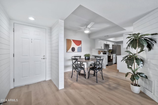 dining area with ceiling fan, light hardwood / wood-style flooring, and wood walls