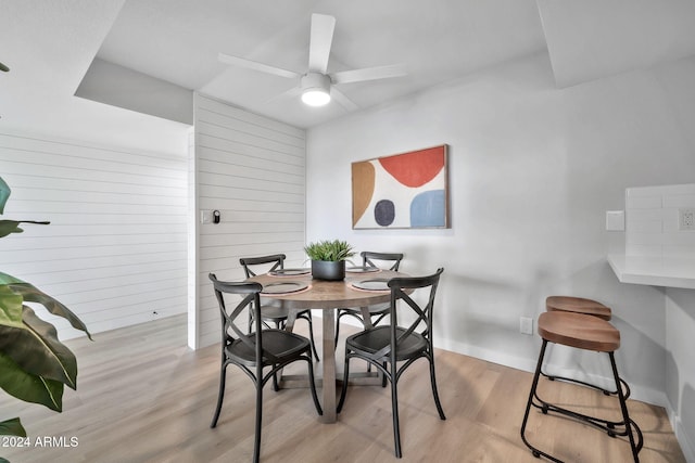 dining space with ceiling fan, light hardwood / wood-style floors, and wooden walls