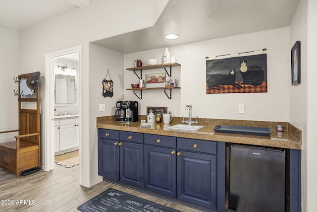 bar featuring sink, blue cabinetry, stainless steel refrigerator, and light wood-type flooring