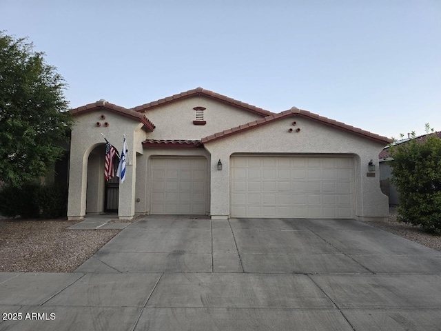 mediterranean / spanish house featuring a garage, concrete driveway, stucco siding, and a tile roof