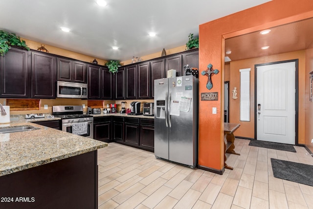 kitchen featuring light stone countertops, appliances with stainless steel finishes, light wood-type flooring, dark brown cabinets, and sink