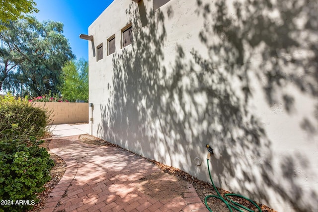 view of side of property featuring stucco siding, a patio, and fence