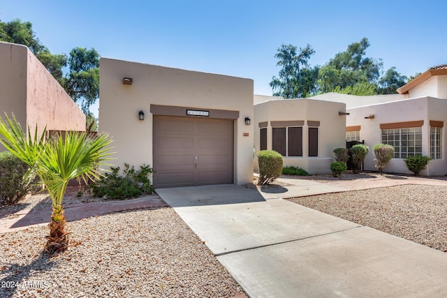 pueblo-style home with stucco siding, a garage, and driveway