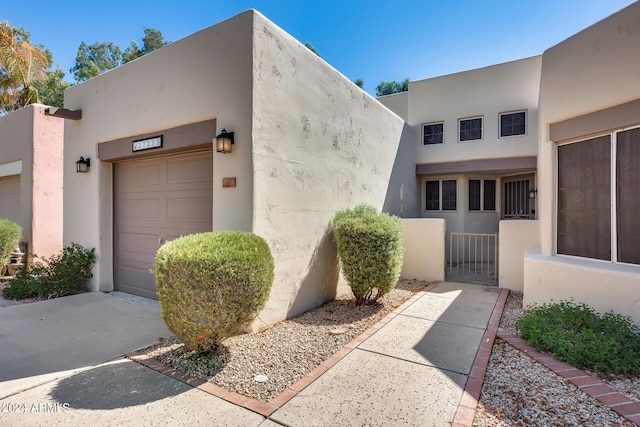 exterior space with stucco siding, an attached garage, and a gate