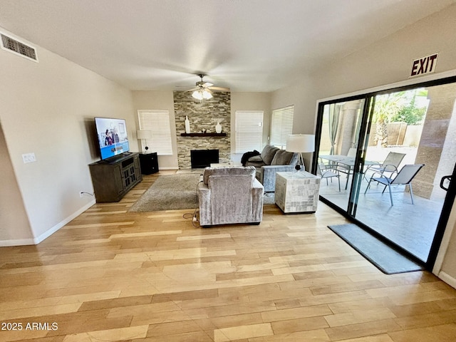 living room with ceiling fan, a stone fireplace, and light hardwood / wood-style flooring