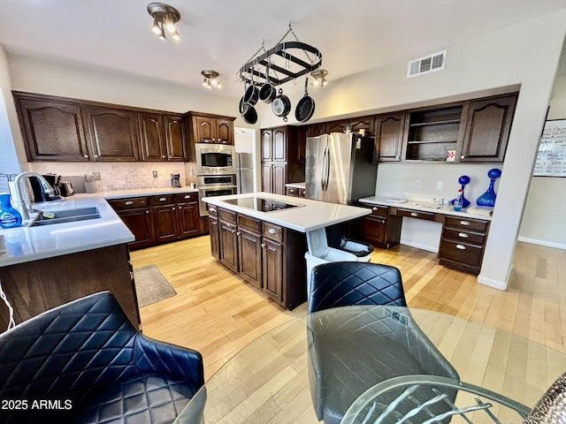 kitchen with appliances with stainless steel finishes, dark brown cabinets, sink, light hardwood / wood-style flooring, and a center island