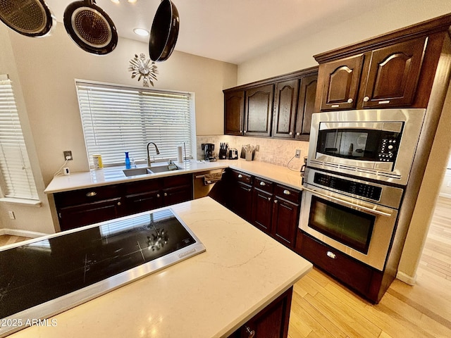 kitchen featuring appliances with stainless steel finishes, light wood-type flooring, tasteful backsplash, dark brown cabinetry, and sink