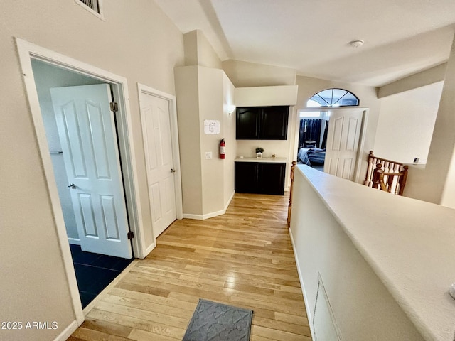 corridor with light hardwood / wood-style floors and lofted ceiling