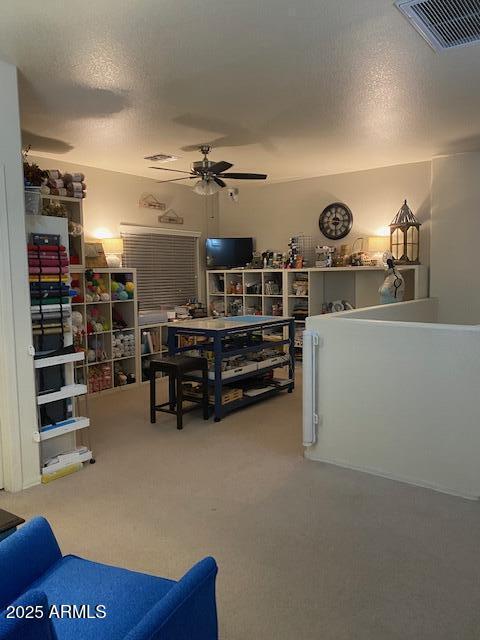 interior space with a ceiling fan, visible vents, a textured ceiling, and carpet flooring