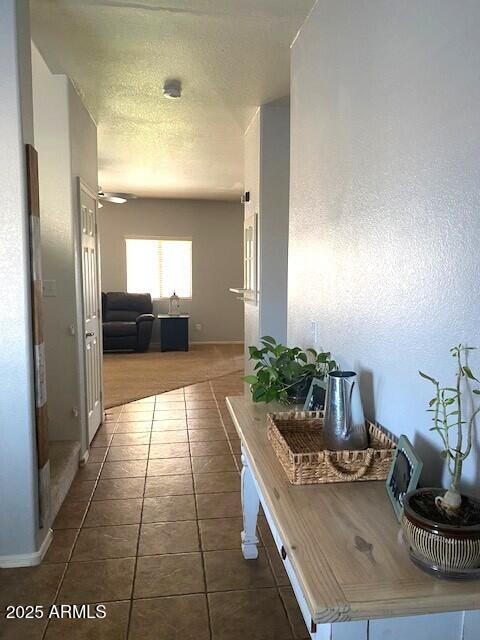 hall with a textured ceiling, baseboards, and dark tile patterned floors