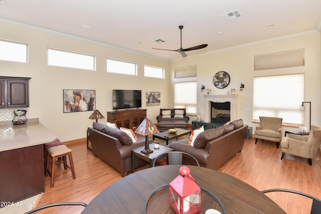 living room with light hardwood / wood-style floors, crown molding, a premium fireplace, and ceiling fan