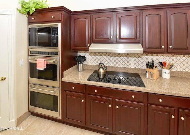 kitchen with light tile patterned flooring, black appliances, decorative backsplash, and light stone countertops