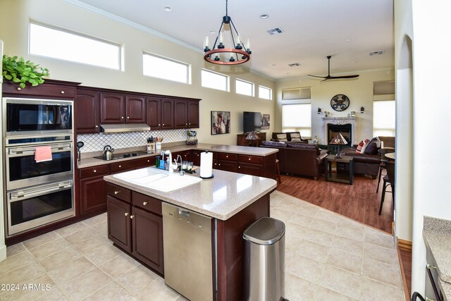 kitchen featuring stainless steel appliances, ceiling fan with notable chandelier, decorative backsplash, light hardwood / wood-style floors, and a kitchen island with sink