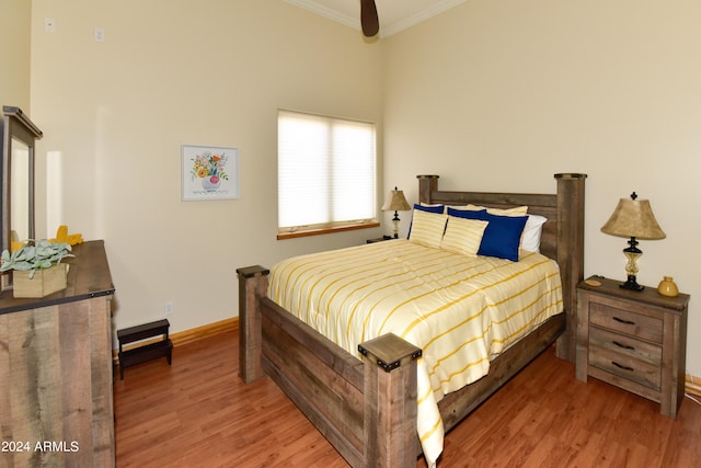 bedroom featuring hardwood / wood-style flooring, crown molding, and a high ceiling