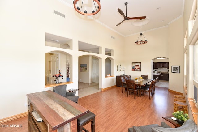 dining space featuring crown molding, ceiling fan with notable chandelier, tile patterned floors, and a towering ceiling