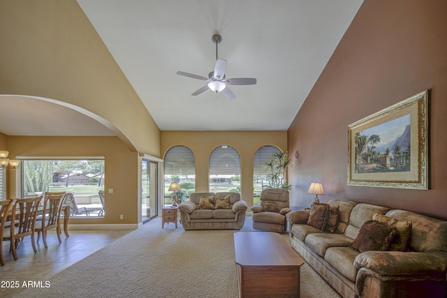 living area featuring ceiling fan, high vaulted ceiling, arched walkways, baseboards, and light carpet