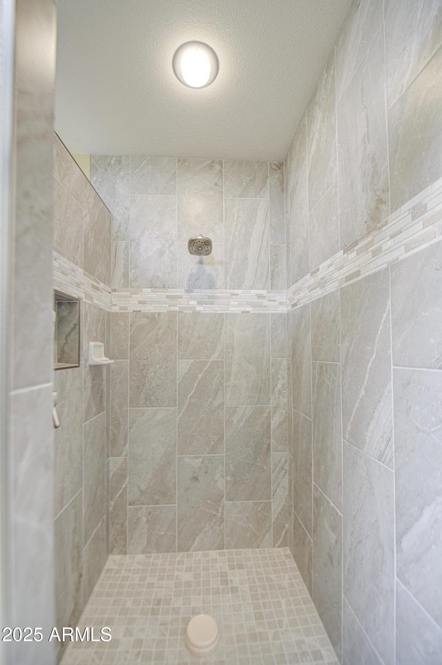 full bathroom with tiled shower and a textured ceiling