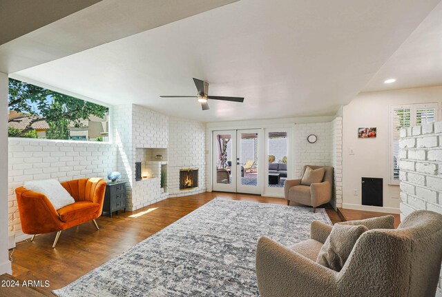 living room featuring hardwood / wood-style flooring, ceiling fan, a brick fireplace, and brick wall