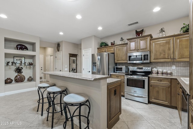kitchen with a kitchen island, a kitchen bar, visible vents, appliances with stainless steel finishes, and tasteful backsplash